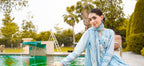 Woman in a light blue traditional outfit by a pool with flowers.
